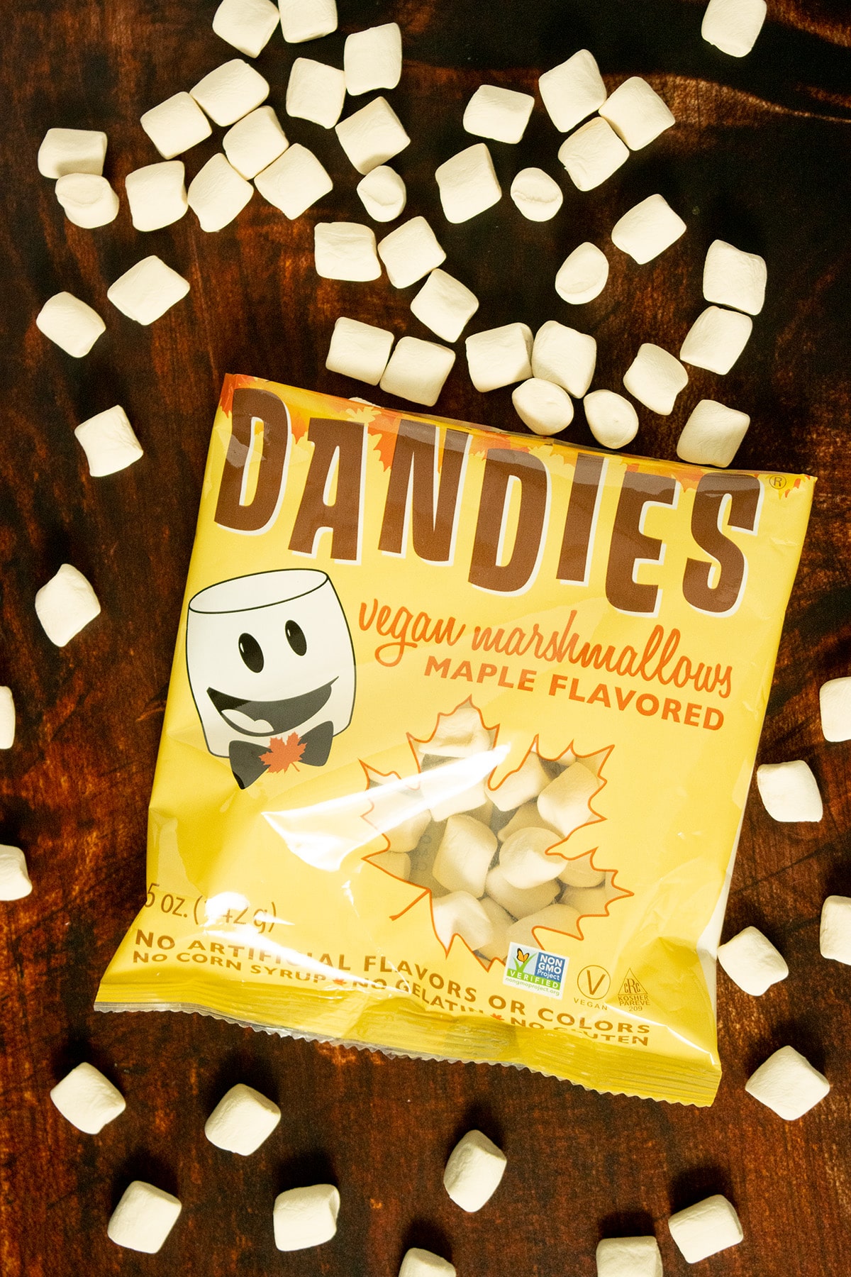 open bag of Dandie's Maple-Flavored Marshmallows on a wooden table. Marshmallows are spilling out all over