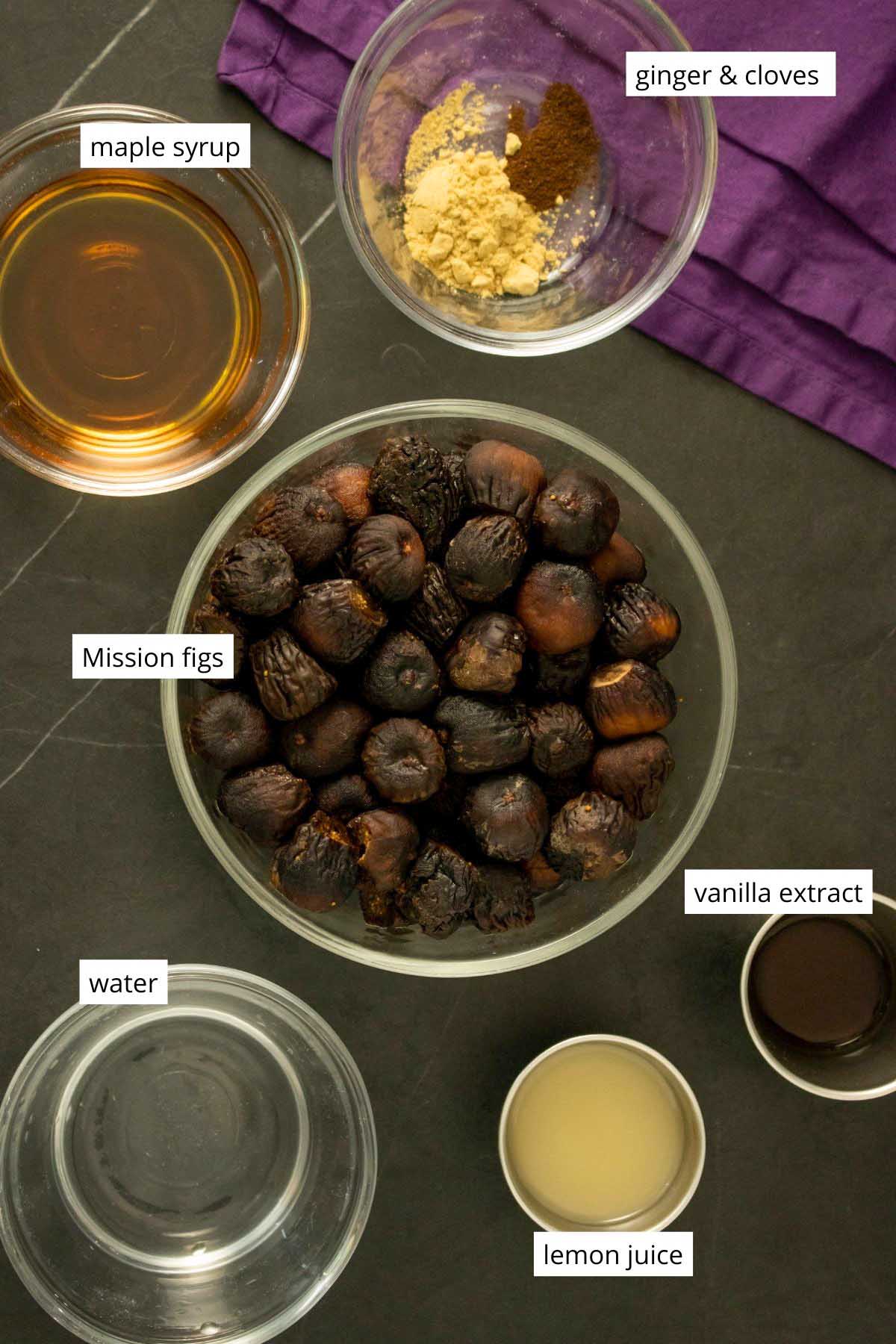 Mission figs in a bowl on a table surrounded by bowls with the other jam ingredients. Text labels on each ingredient.