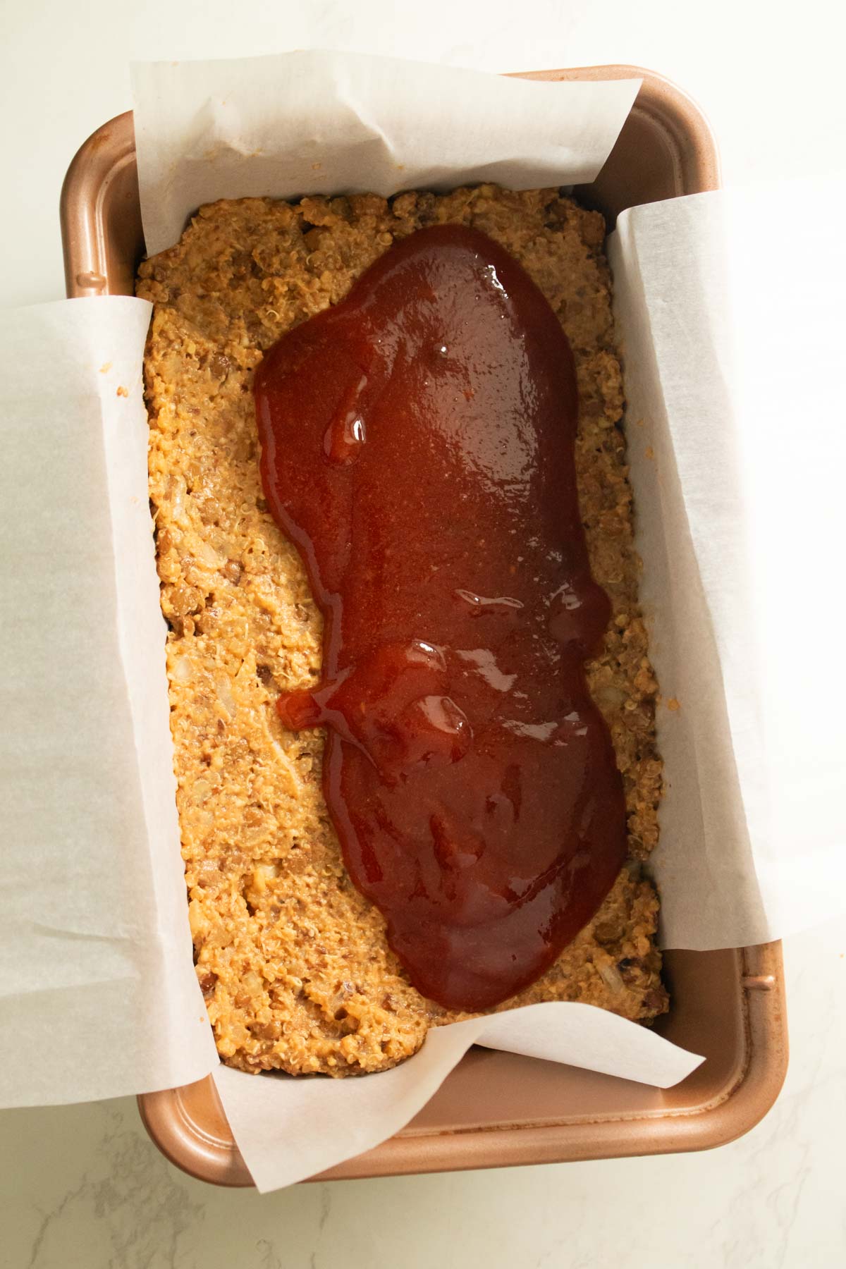 pouring ketchup glaze onto the quinoa lentil meatloaf mixture