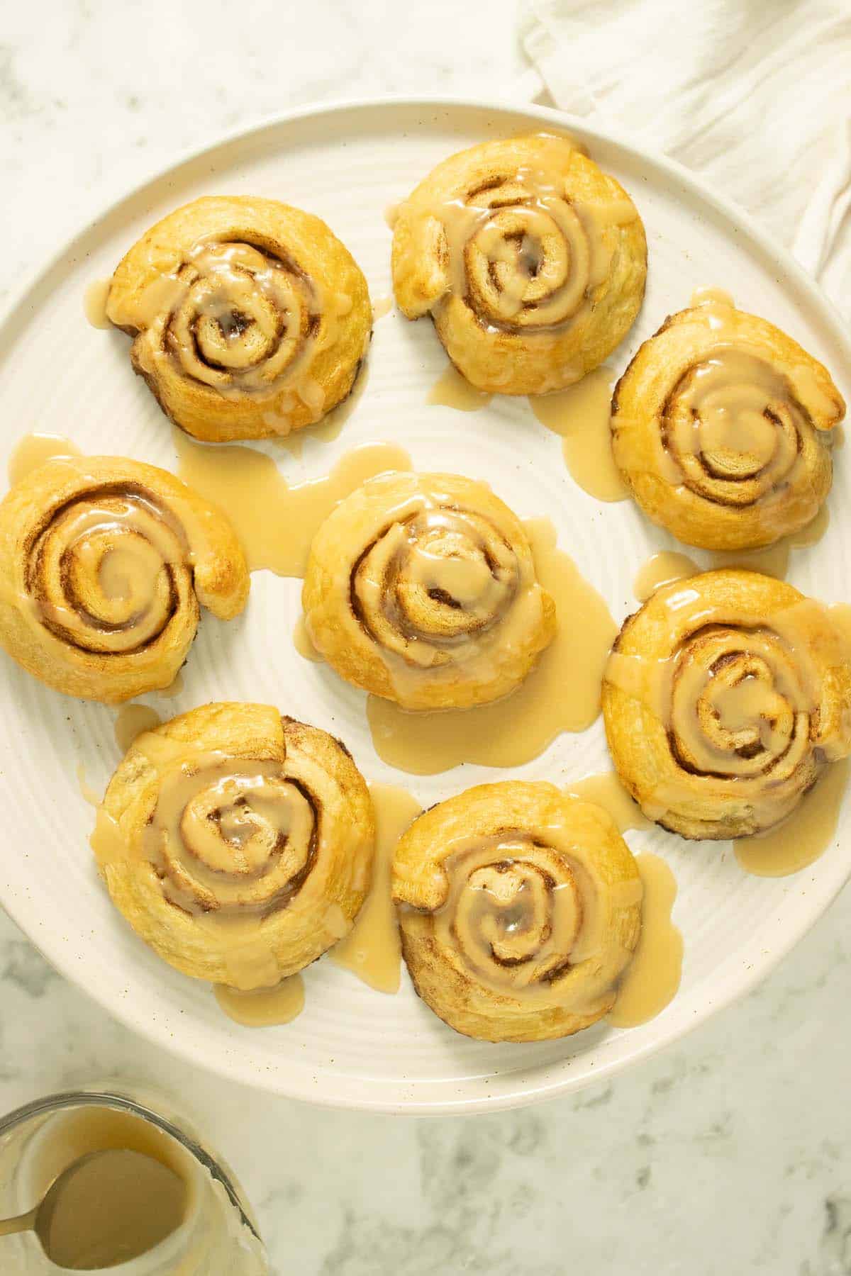 overhead shot of 8 vegan cinnamon rolls on a serving plate with maple icing