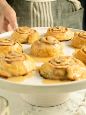 person serving vegan cinnamon rolls on a serving plate with maple icing