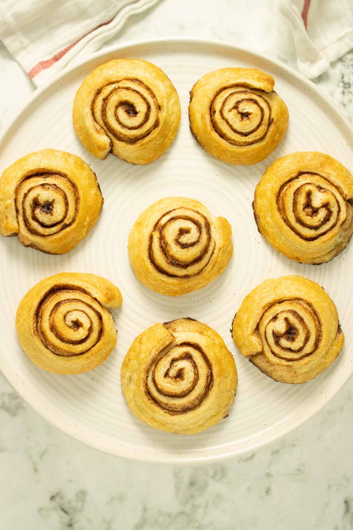 overhead shot of 8 vegan cinnamon rolls on a serving plate, unfrosted