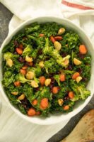 kale and broccoli salad with cranberries and macadamia nuts in a white bowl on tea towel