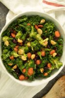 kale and broccoli salad with cranberries and macadamia nuts in a white bowl on tea towel