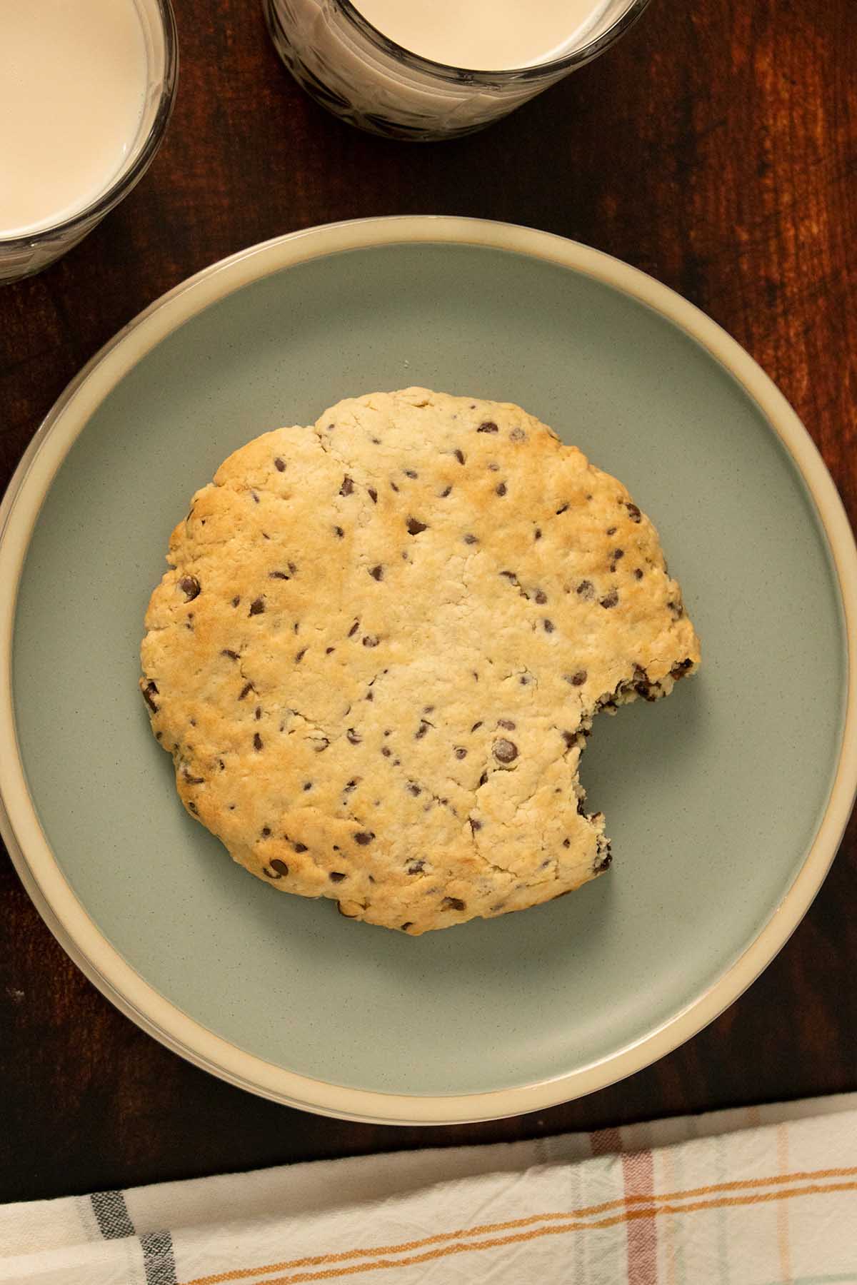 giant, vegan air fryer cookie with a bite taken out on a plate with glasses of soy milk next to it