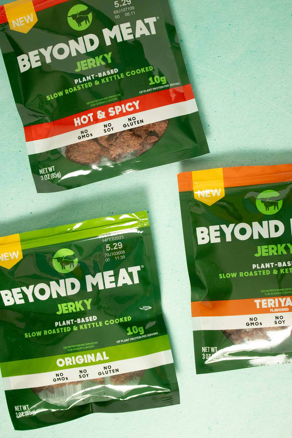 3 bags of Beyond Meat Jerky on a blue table: original, teriyaki and hot & spicy flavors