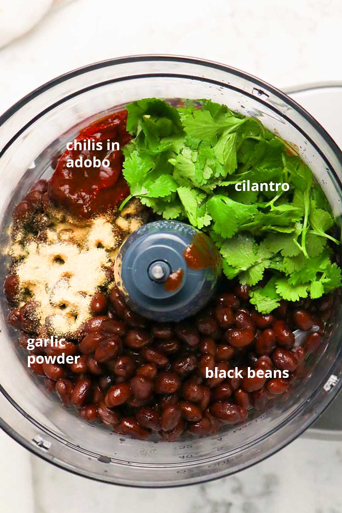 vegan black bean dip ingredients in the food processor with text labels on them