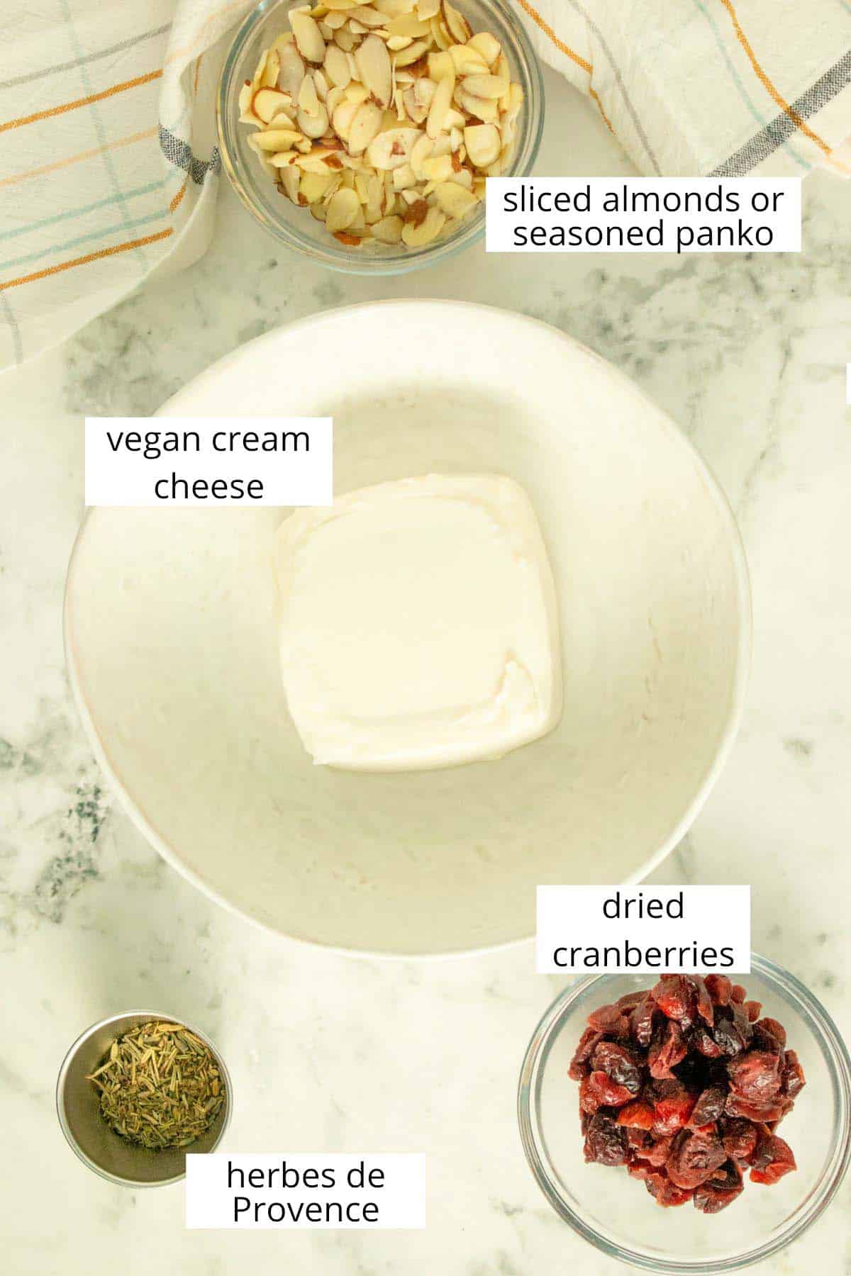 vegan cream cheese, herbs, cranberries, and almonds in bowls on a white table