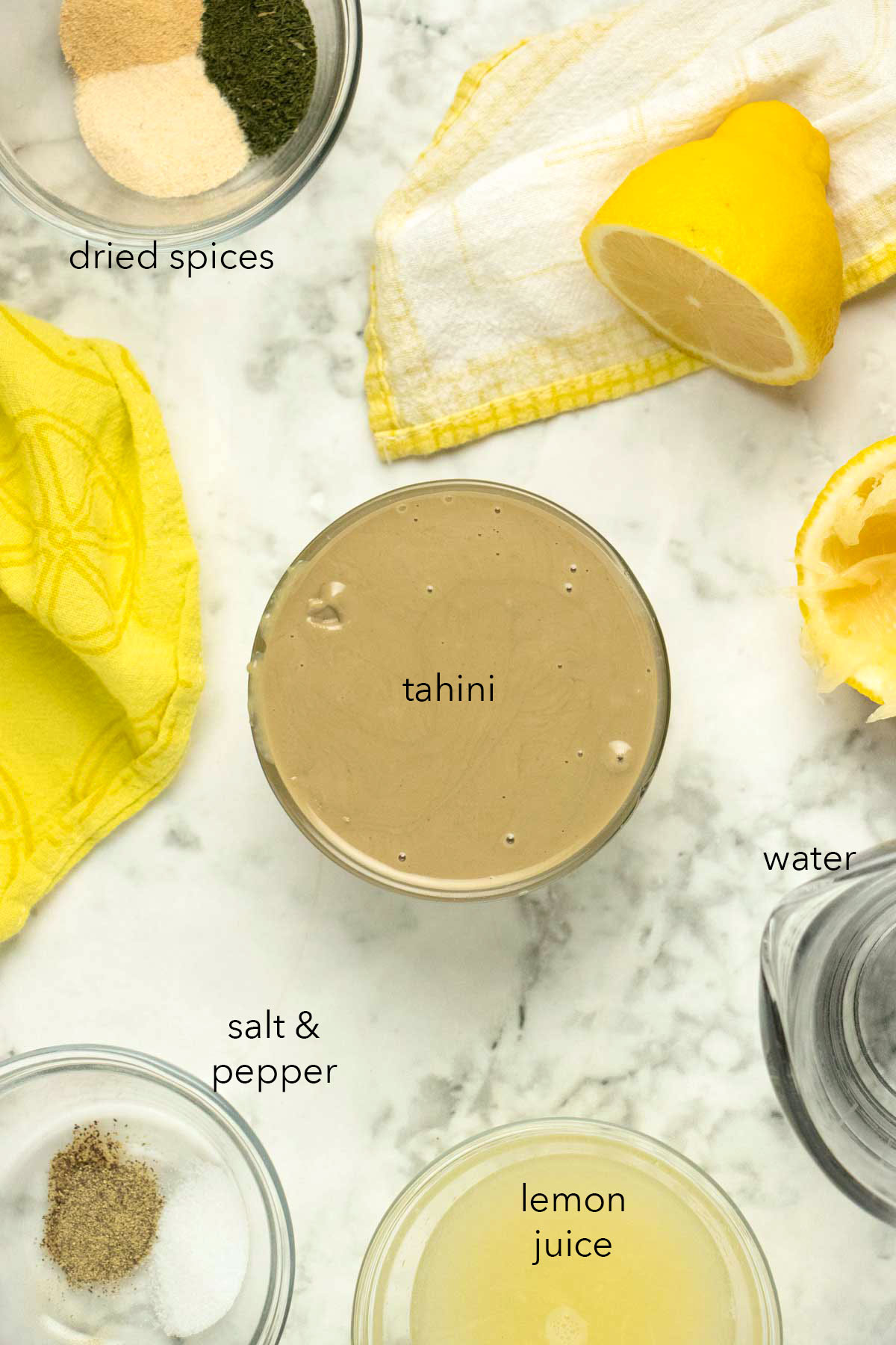 bowl of tahini surrounded by lemon and spices on a marble table