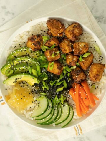 tofu sushi bowl with fresh veggies, pickled ginger, and sesame seeds on a marble table