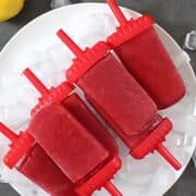 cherry lemonade popsicles on a white plate with ice cubes
