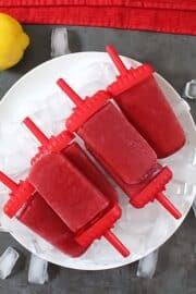 cherry lemonade popsicles on a white plate with ice cubes