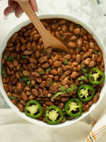 Instant Pot Pinto Beans in a white bowl with a spoon, jalapeños, and cilantro