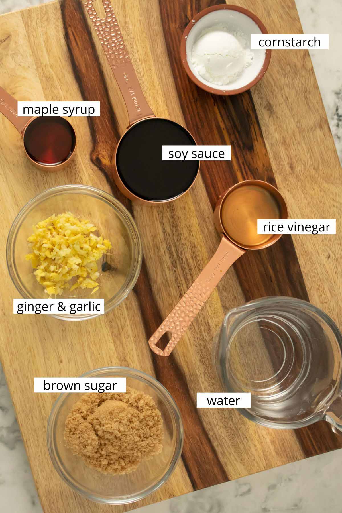 teriyaki tofu ingredients in bowls and measuring spoons on a wooden cutting board with text labels on each item