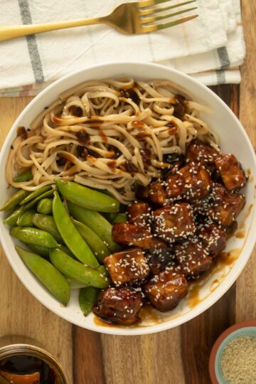 baked teriyaki tofu in a bowl with noodles and roasted pea pods