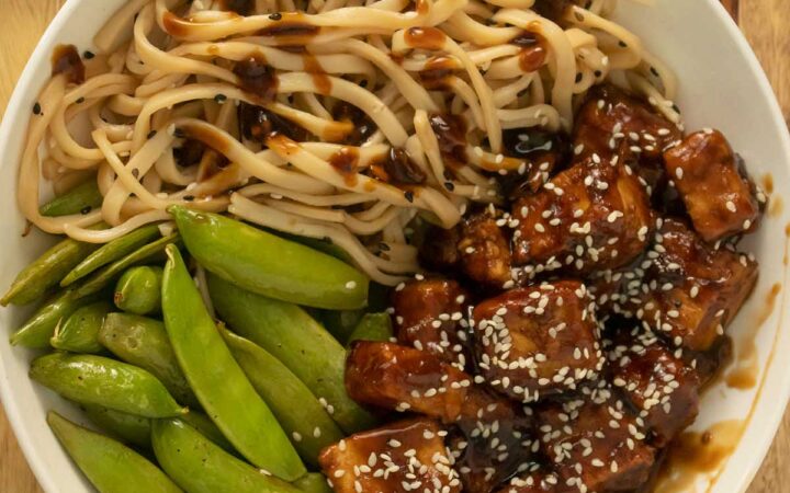 baked teriyaki tofu in a bowl with noodles and roasted pea pods