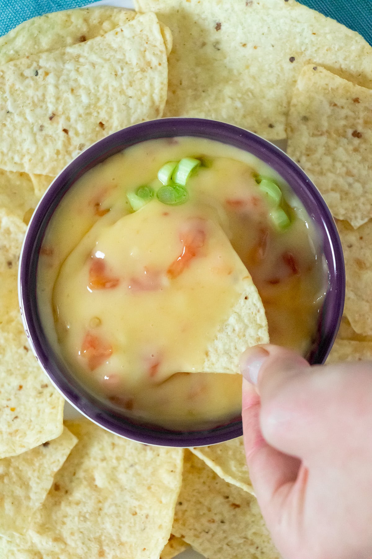 hand dipping a chip into vegan queso