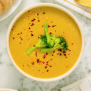 bowl of creamy vegan broccoli soup topped with steamed broccoli and red pepper flakes