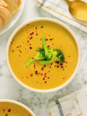 bowl of creamy vegan broccoli soup topped with steamed broccoli and red pepper flakes