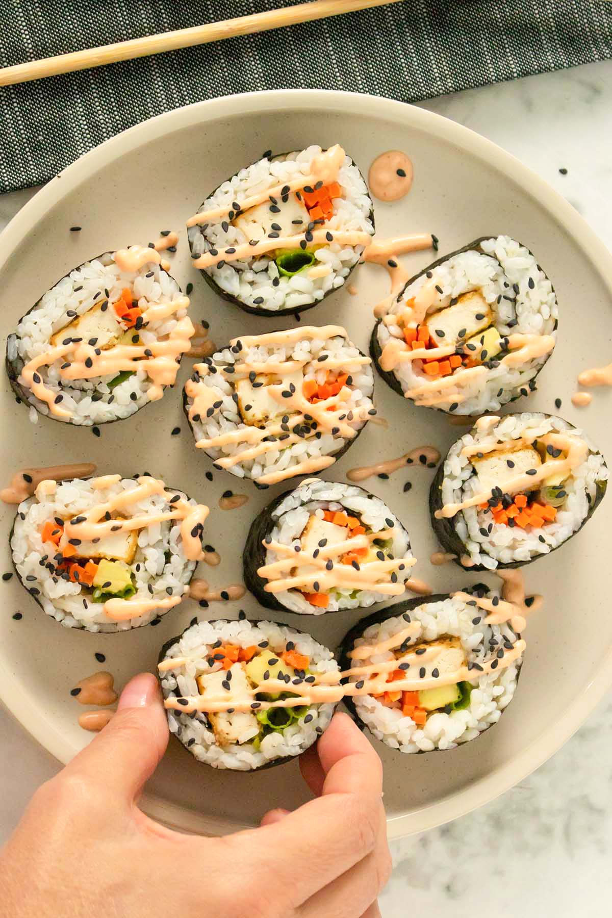 plate of tofu sushi topped with sriracha mayo and black sesame seeds