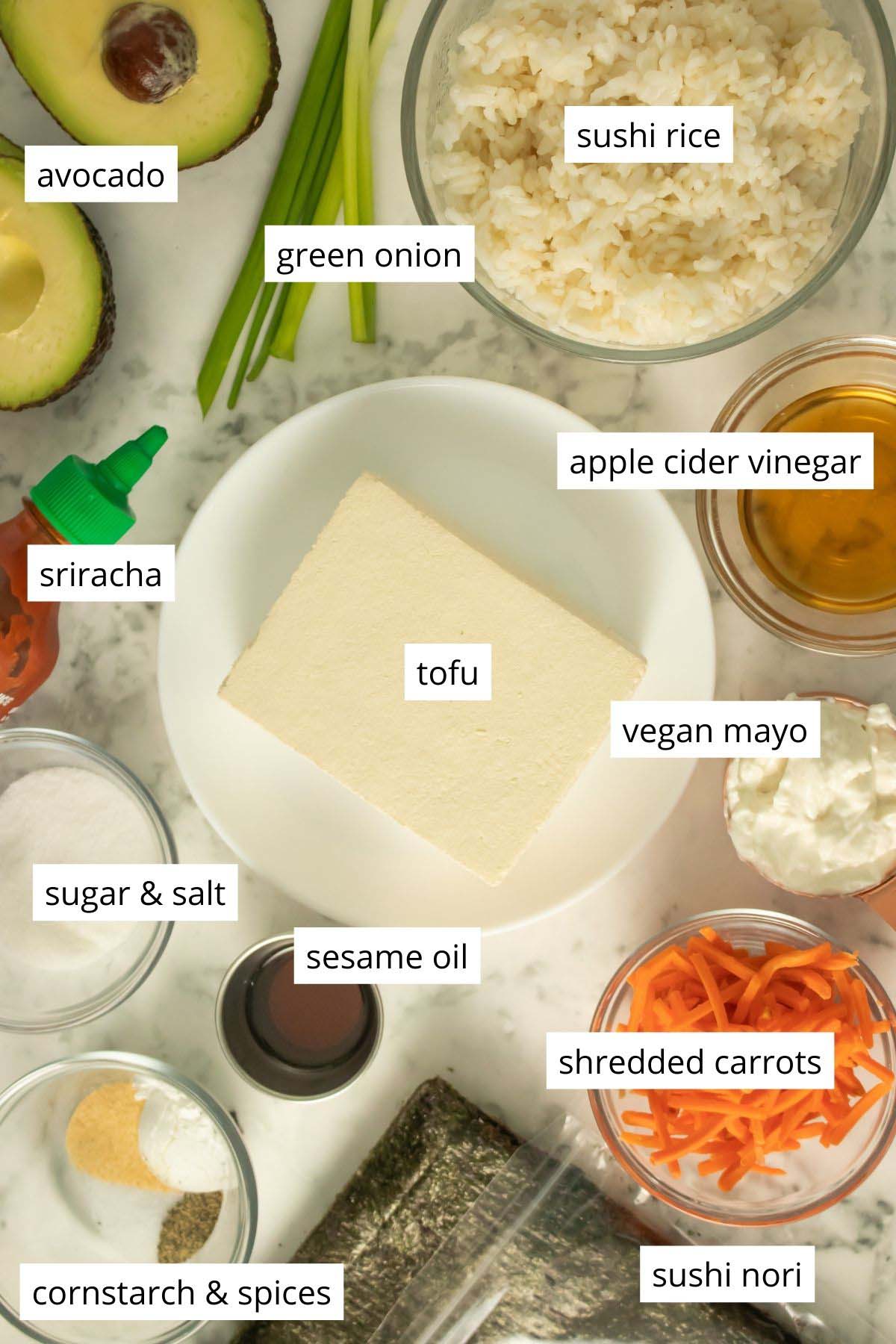 tofu, veggies, sushi rice, nori sheets, and seasonings arranged on a marble table