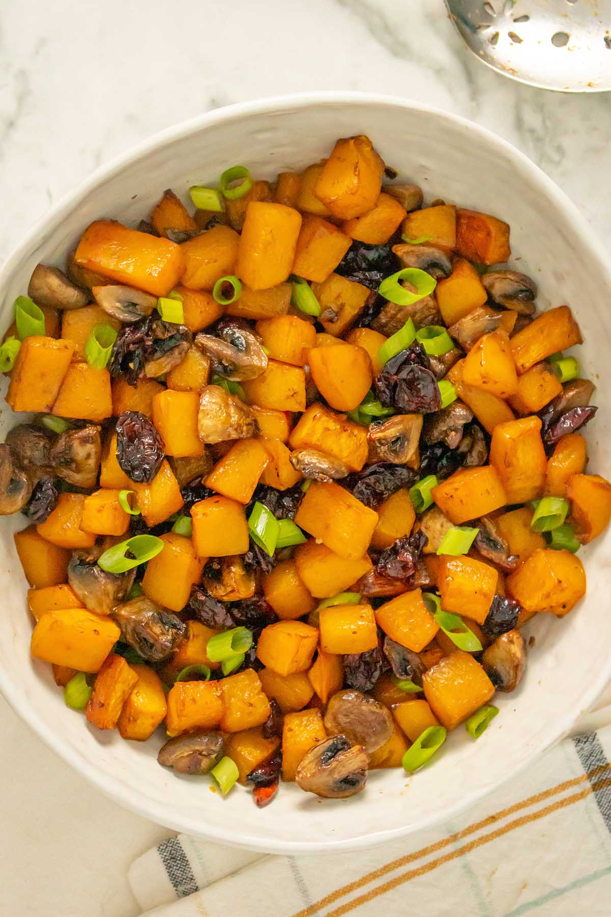 serving bowl of butternut squash and mushrooms with green onion and cranberry