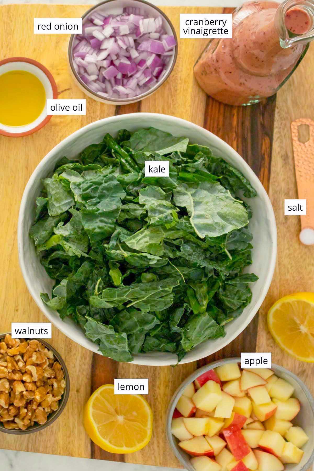 bowl of raw kale surrounded by other salad ingredients on a wooden cutting board