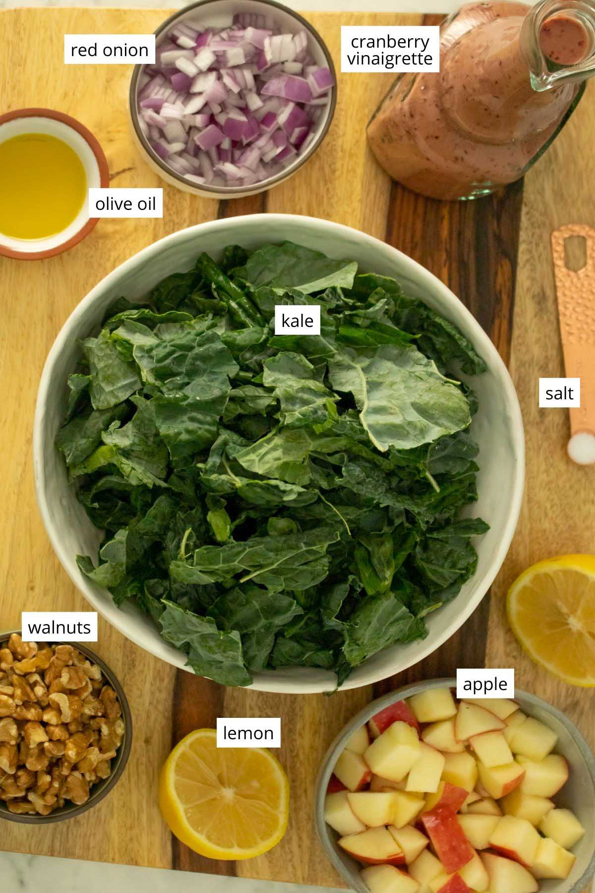 bowl of raw kale surrounded by other salad ingredients on a wooden cutting board