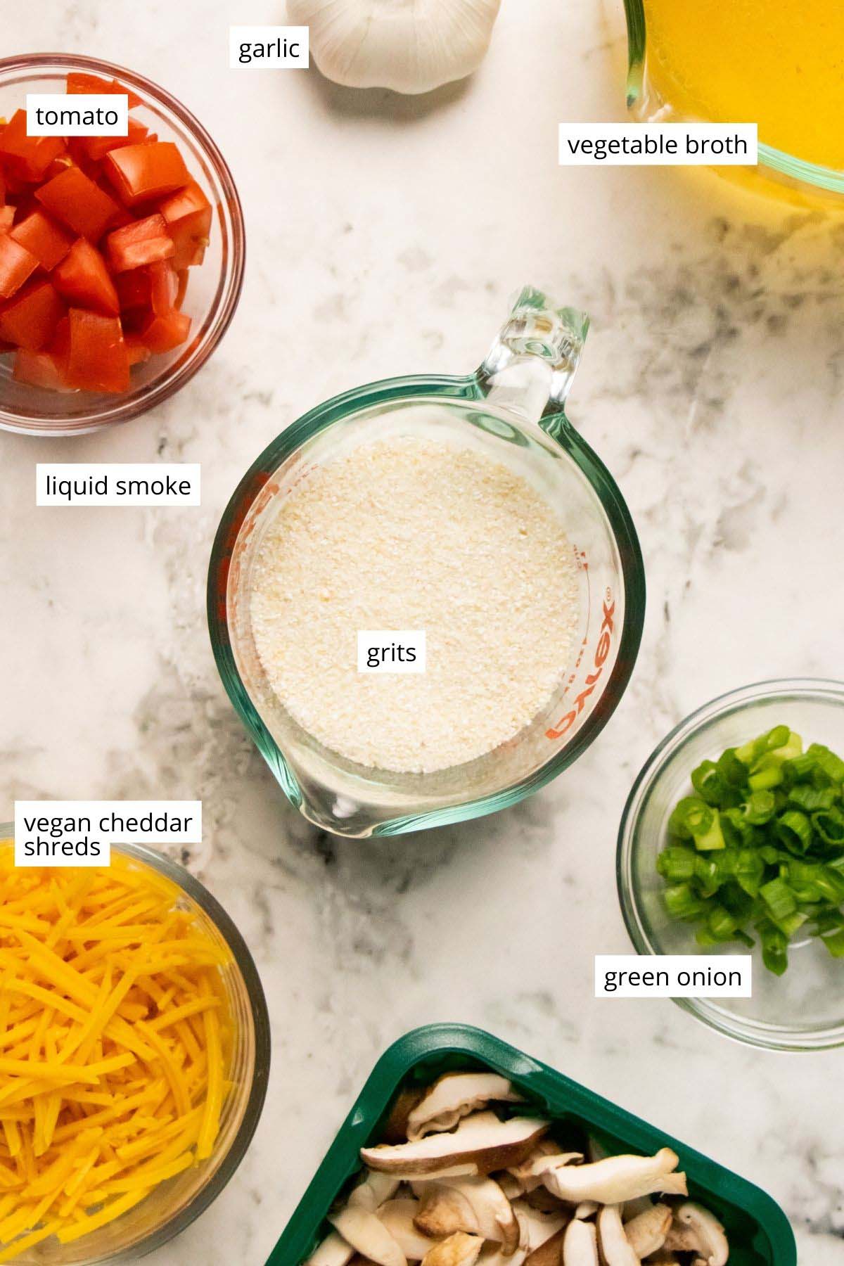 grits, vegan cheese, veggies, and other ingredients in cups and bowls on a marble tabletop