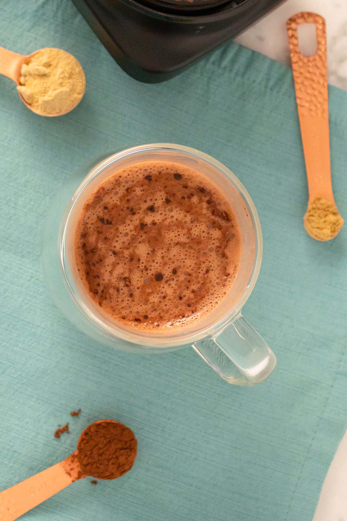 maca hot chocolate in a mug on a table surrounded by measuring spoons of powdered ingredients