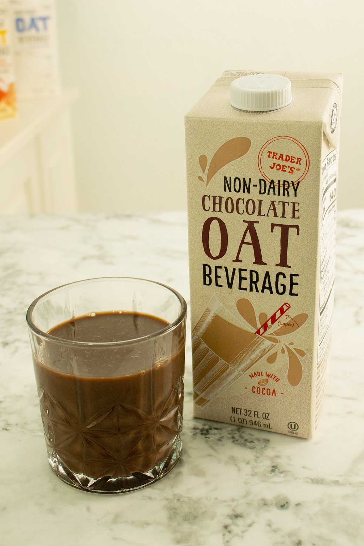 glass of Trader Joe's chocolate oat milk next to the carton