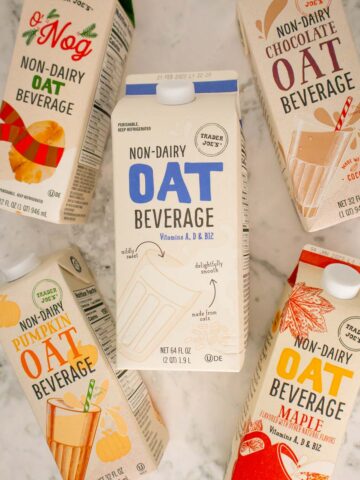 Trader Joe's Oat milk carton surrounded by their oat nog, maple beverage, chocolate, and pumpkin varieties