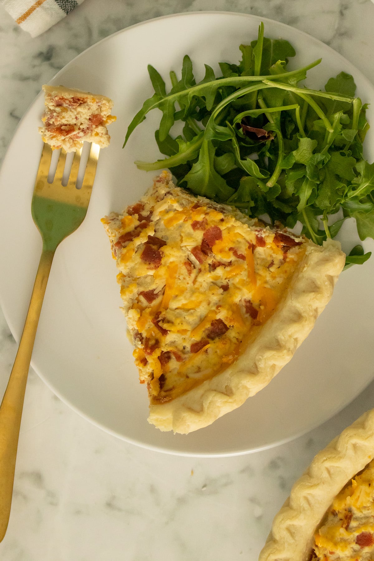 vegan quiche Lorraine on a white plate with a salad. A bite is on a fork.