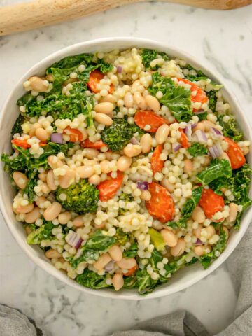 Israeli couscous salad with carrots, broccoli, kale, and white beans in a white bowl