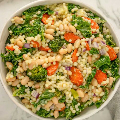 Israeli couscous salad with carrots, broccoli, kale, and white beans in a white bowl