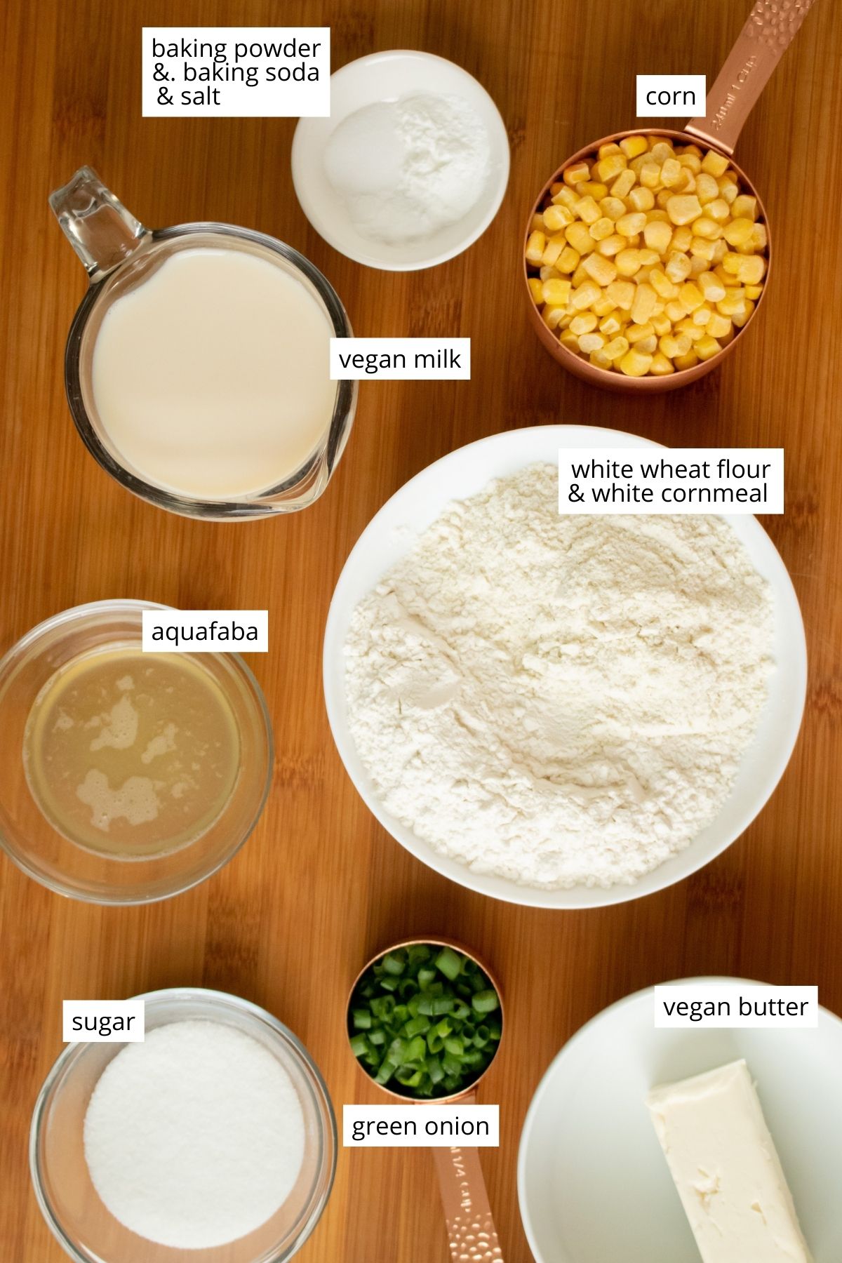 white cornmeal, flour, and other muffin ingredients in bowls on a wooden table