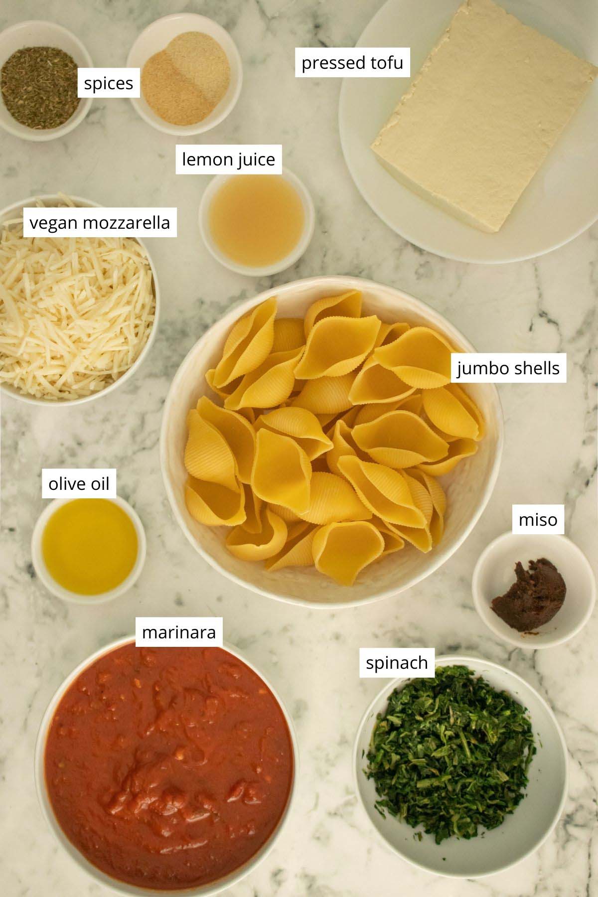 shell pasta, tofu, marinara, vegan cheese, and seasonings in bowls on a white table