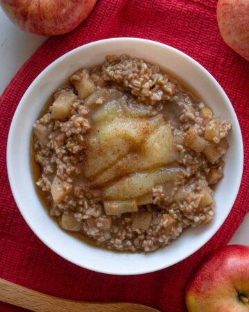 Instant Pot steel cut oats with apple pieces in a white bowl topped with applesauce and maple syrup