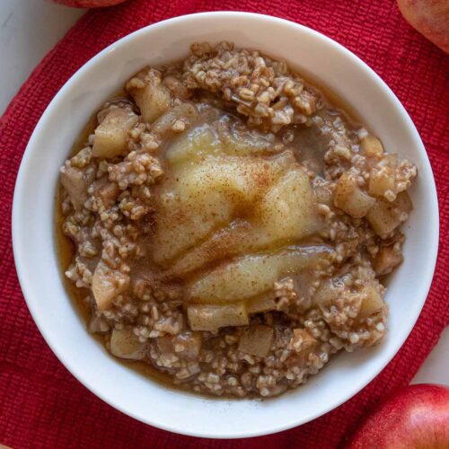 Instant Pot steel cut oats with apple pieces in a white bowl topped with applesauce and maple syrup