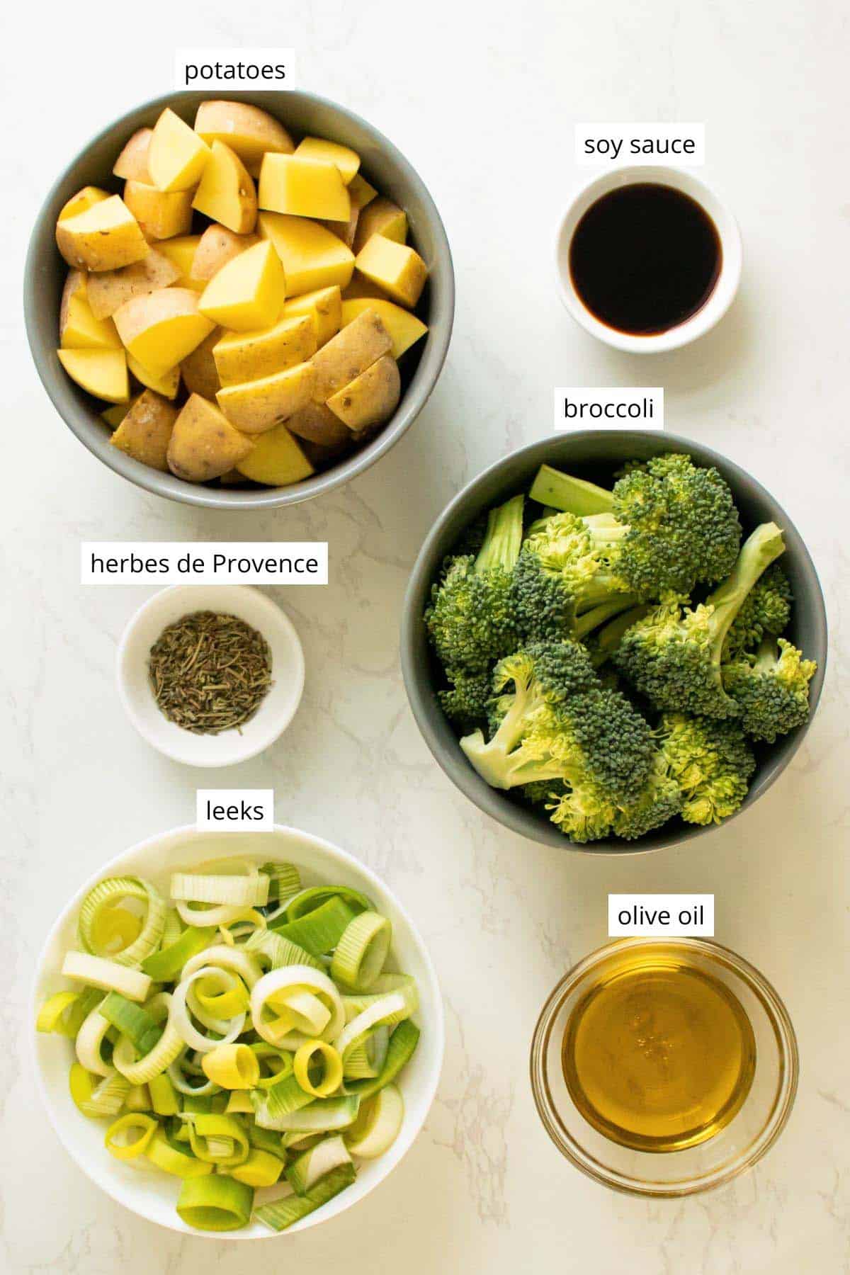 potatoes, broccoli, leeks, oil, herbs, and soy sauce in bowls on a marble table