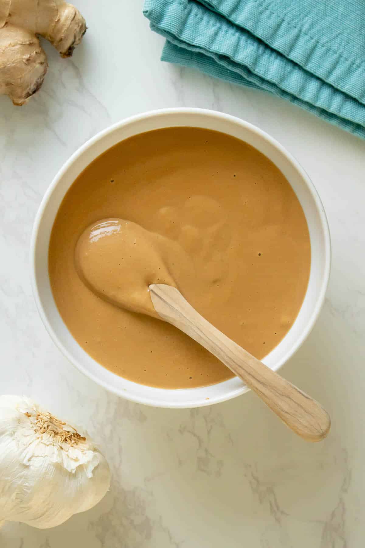 white bowl of tahini miso dressing with a spoon in it, so you can see the creamy texture