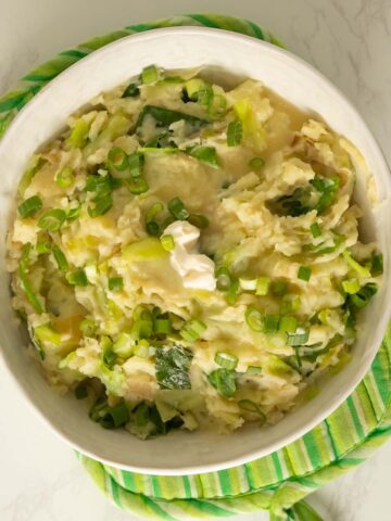 serving bowl of vegan colcannon with a pat of butter and green onions on it