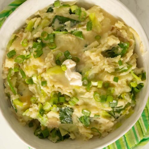 serving bowl of vegan colcannon with a pat of butter and green onions on it