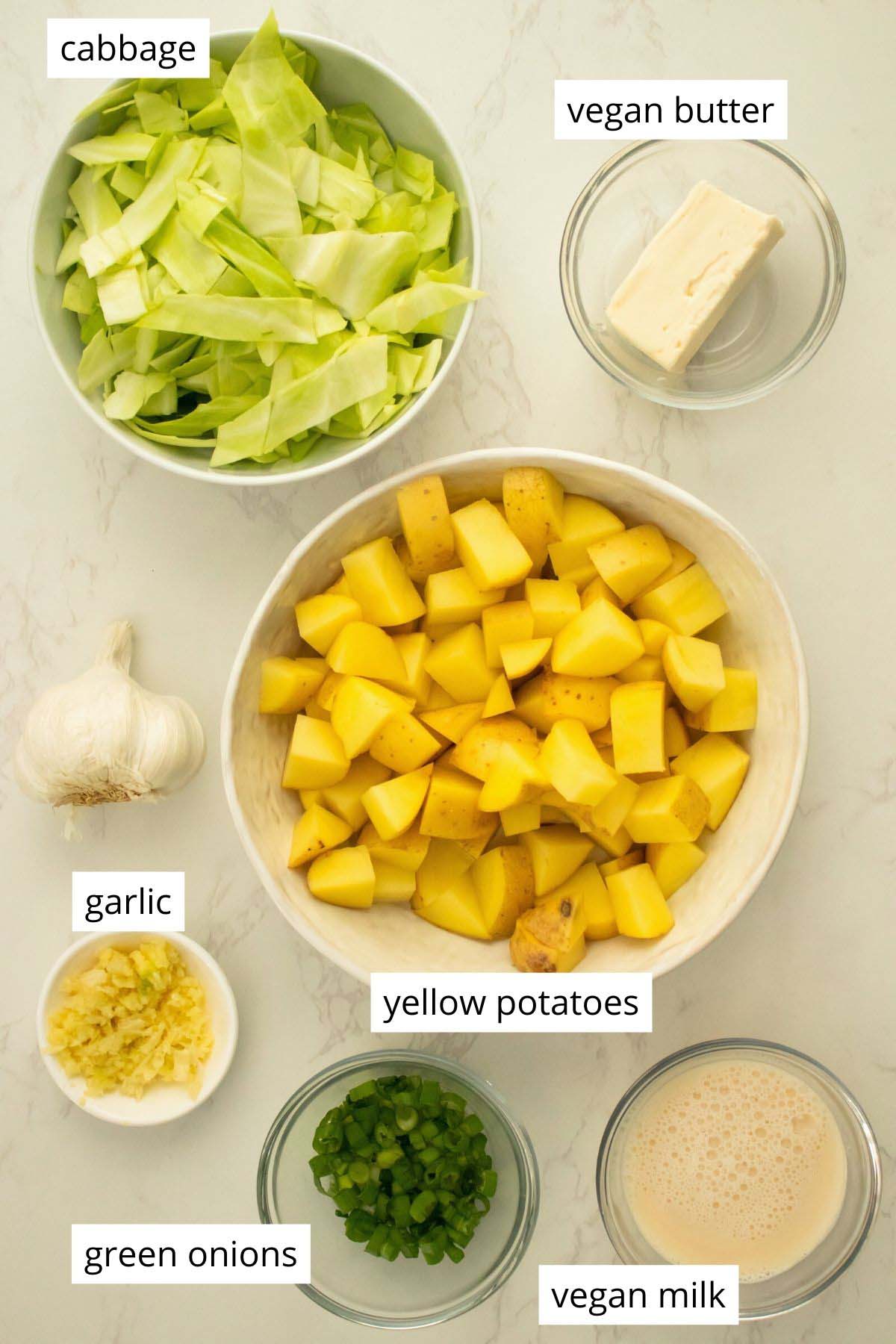 potatoes, cabbage, and other ingredients in bowls on a white table, text labels on each ingredient