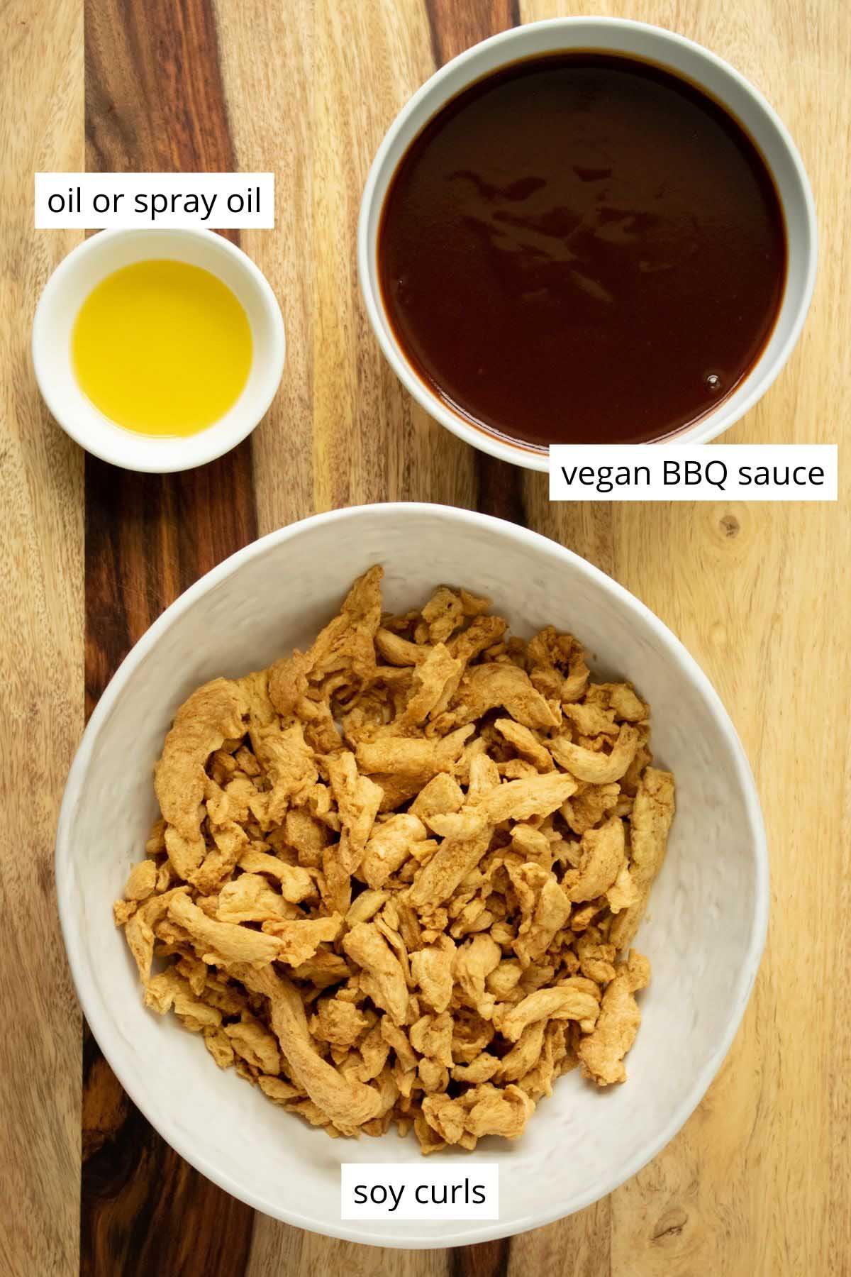 soy curls, BBQ sauce, and oil in bowls on a wooden table