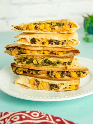 a stack of vegan quesadillas with beans and corn on a white plate