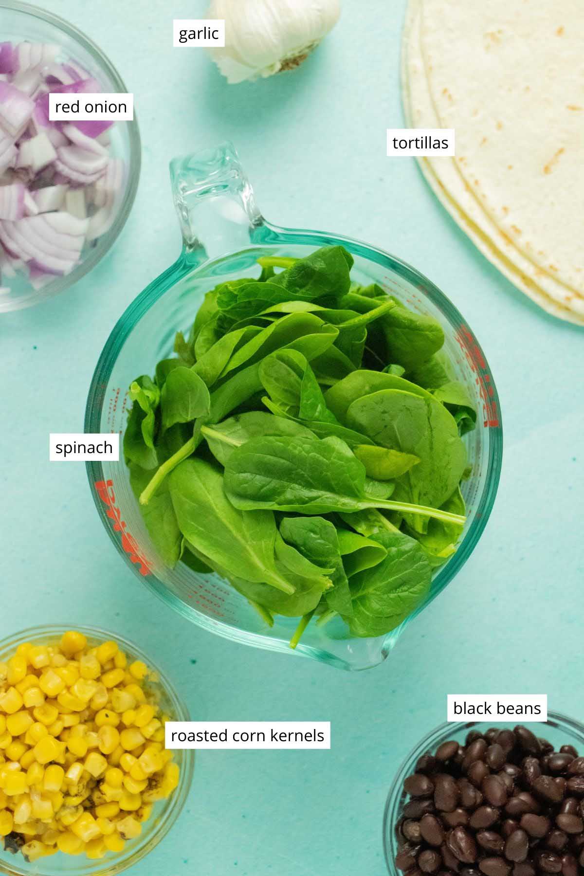 spinach, beans, and other veggies in bowls on a blue table