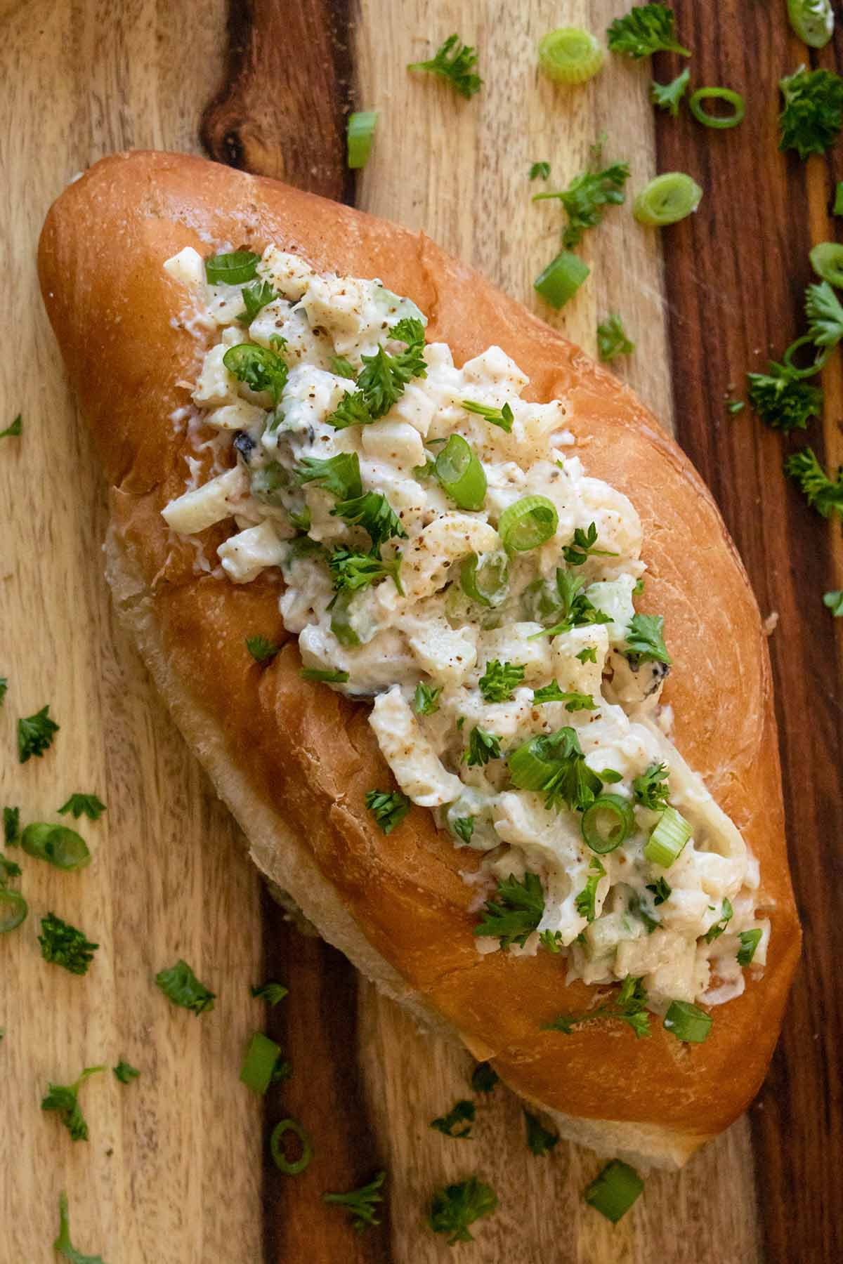 close-up of a vegan lobster roll on a wooden tabletop sprinkled with green onion and parsley