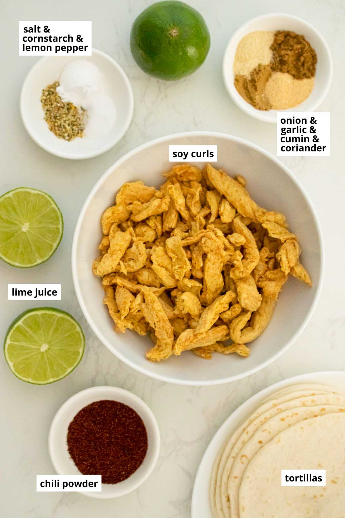 soy curls, tortillas, limes, and spices in bowls on a white table