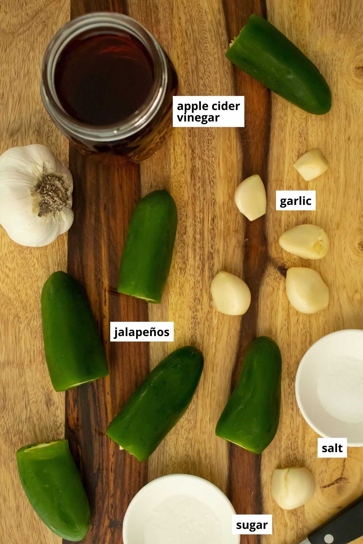 jalapeños, garlic, vinegar, salt, and sugar on a wooden cutting board with text labels on each